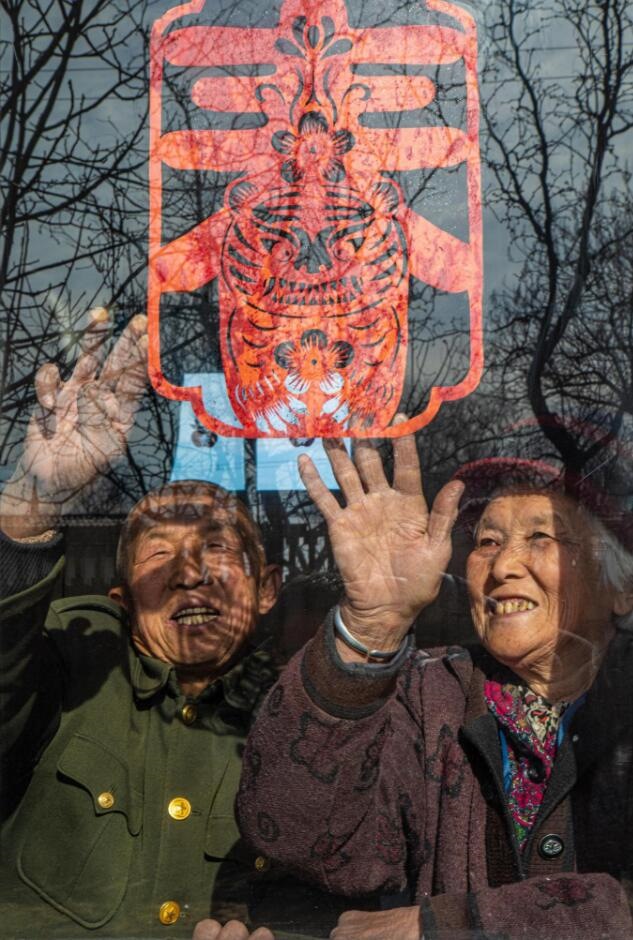 臘月里，霍州市師莊鄉(xiāng)馮南垣村村民師榮光(左)在災(zāi)后重建的新家里貼窗花。(霍州市委宣傳部供圖)