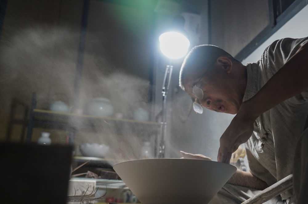 ↑ 在景德鎮(zhèn)，手工匠人吹去坯內(nèi)的泥土（2021年7月14日攝）。