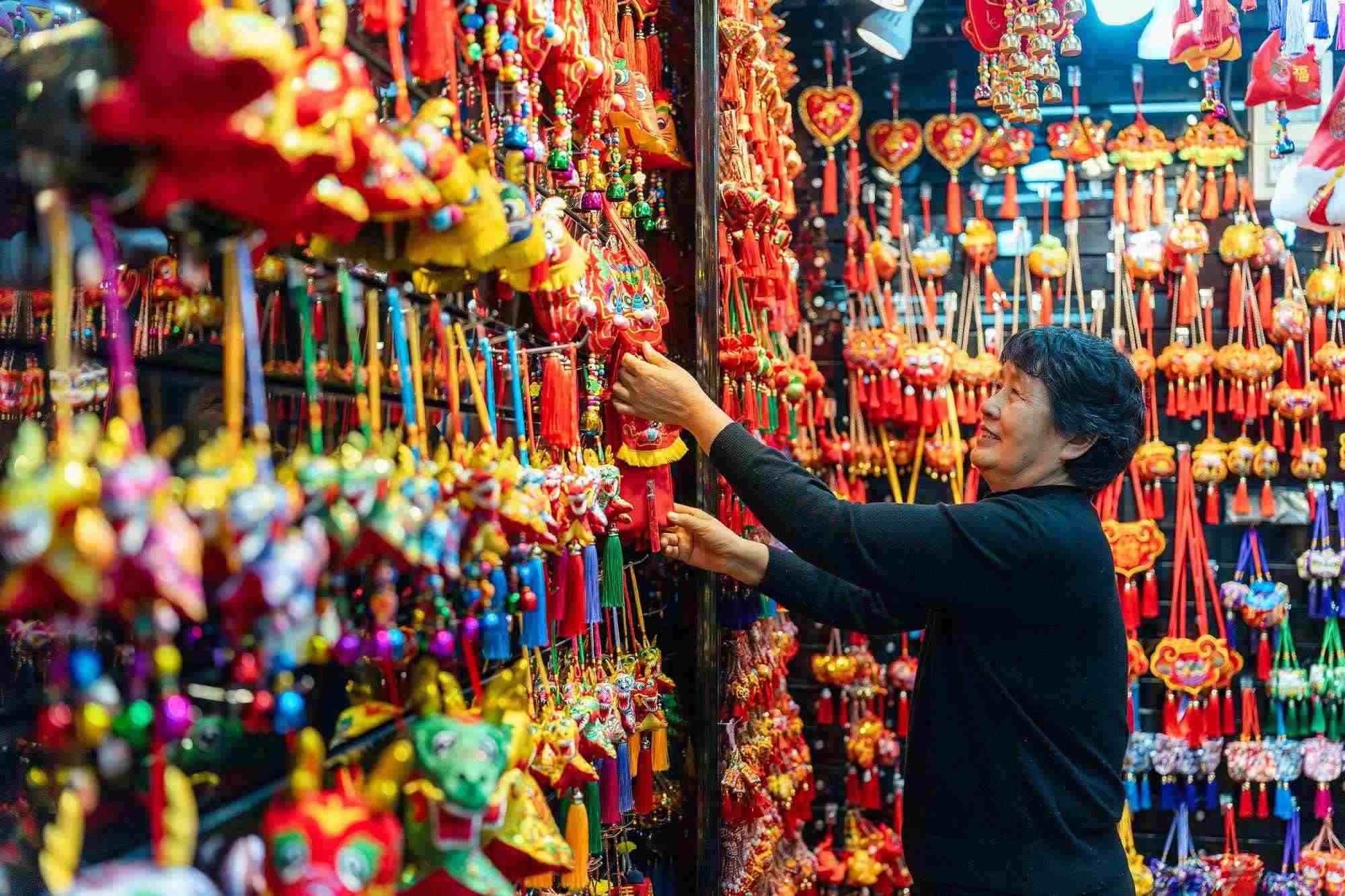 2023年12月11日，金華義烏國際商貿(mào)城，龍年喜慶用品掛滿攤位，顧客正在挑選中。