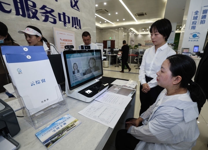 在浙江省嘉興市秀洲區(qū)王江涇鎮(zhèn)便民服務(wù)中心的“跨域通辦·云綜窗”窗口，辦理開業(yè)登記的個(gè)體工商戶（右一）通過該系統(tǒng)與江蘇省蘇州市吳江區(qū)盛澤鎮(zhèn)行政審批局工作人員視頻連線，進(jìn)行身份讀取及材料線上審核（2024年5月9日攝）。新華社記者 徐昱 攝