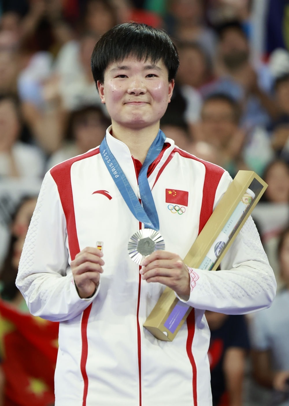 巴黎奧運(yùn)會羽毛球女子單打亞軍、中國選手何冰嬌在頒獎儀式上一手握著銀牌，一手握著西班牙奧委會徽章（2024年8月5日攝）。新華社記者 任正來 攝