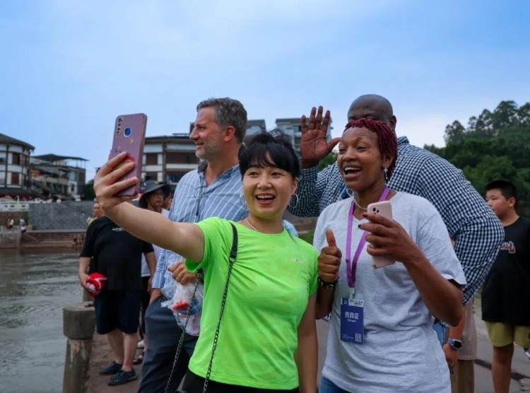 2024“一帶一路”媒體合作論壇聯(lián)合采訪調(diào)研行成員在樂山蘇稽古鎮(zhèn)與游客合影留念。本報記者 伊霄攝