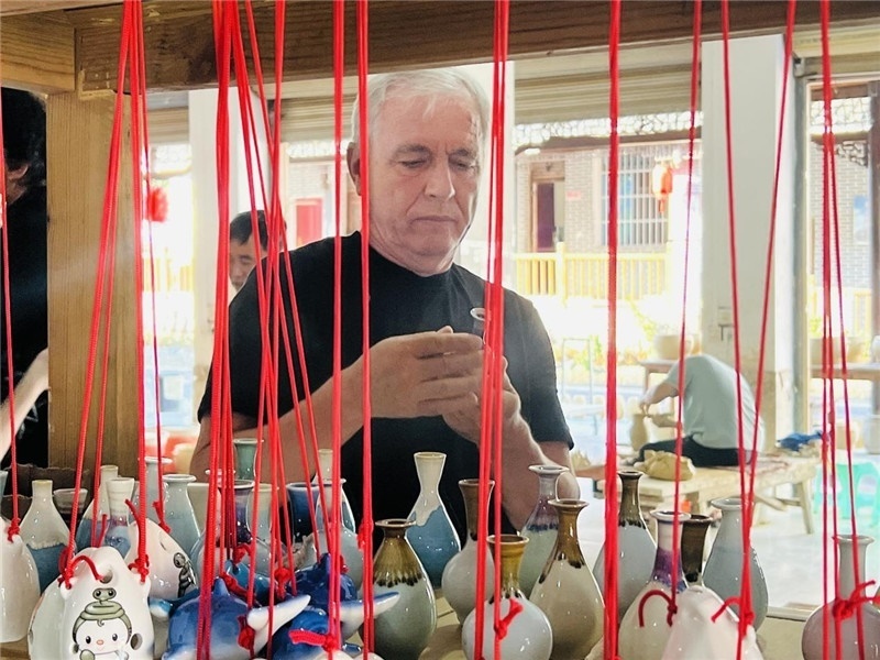 鄉(xiāng)愁如同一根根紅線，將游子與故鄉(xiāng)永遠地牽連到一起?；逄账囄幕瘎?chuàng)意一條街的母氏陶藝館內，紅線吊著陶瓶，思緒游走萬里。摩爾多瓦“信息標簽”通訊社社長亞歷山大·塔納斯端詳著館內展示的陶藝作品，并挑選出心儀的小擺件帶回摩爾多瓦，也帶走花茂村的“鄉(xiāng)愁”。（張亞欣攝）