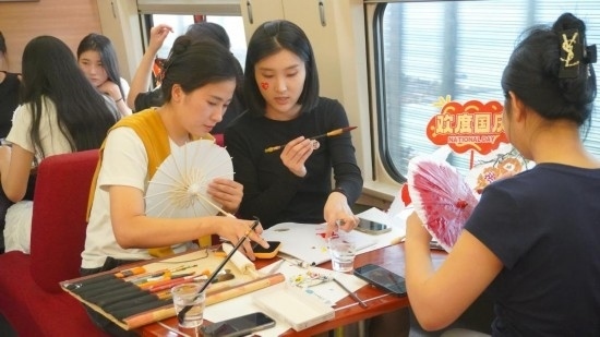 10月1日，旅客們?cè)贕1634次列車(chē)上給油紙傘作畫(huà)。新華社記者周義 攝