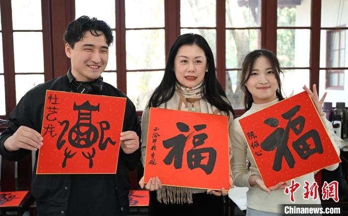 1月20日，外籍留學(xué)生和西泠印社社員李硯(中)展示各自創(chuàng)作的福貼。當(dāng)日，來(lái)自巴西、馬來(lái)西亞、加納、哈薩克斯坦的外籍留學(xué)生在浙江杭州西泠印社體驗(yàn)福貼、春聯(lián)和篆刻，感受古老的中國(guó)傳統(tǒng)文化。中新社記者 王剛 攝